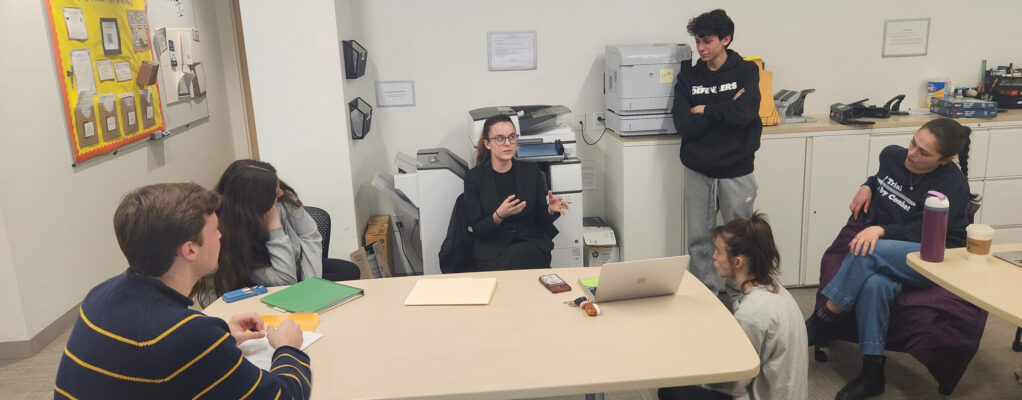 Group of students talking and listening around a table.