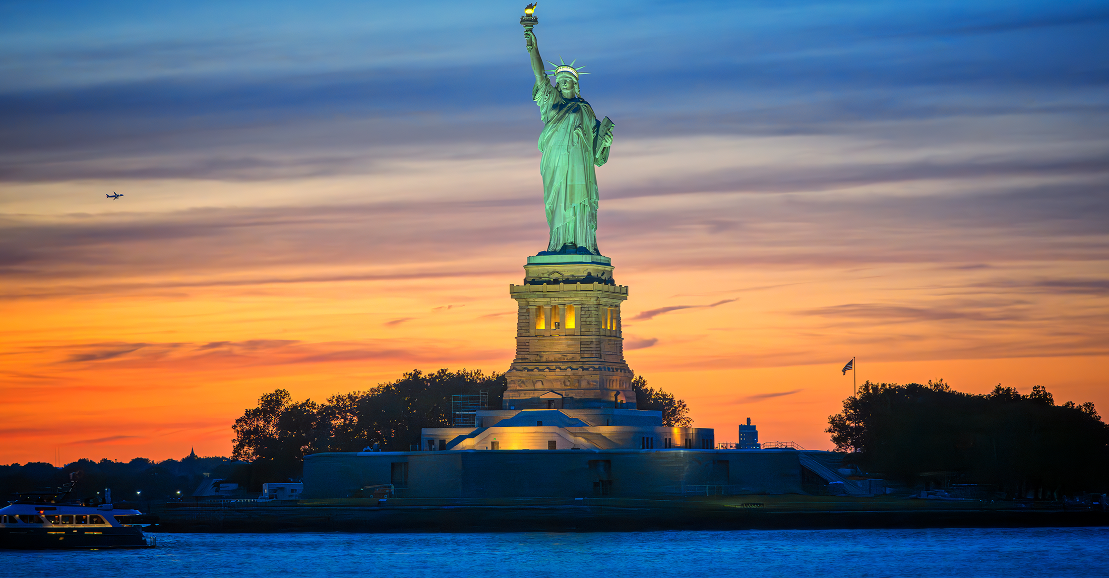 The Statue of Liberty in the forefront of a sunset sky