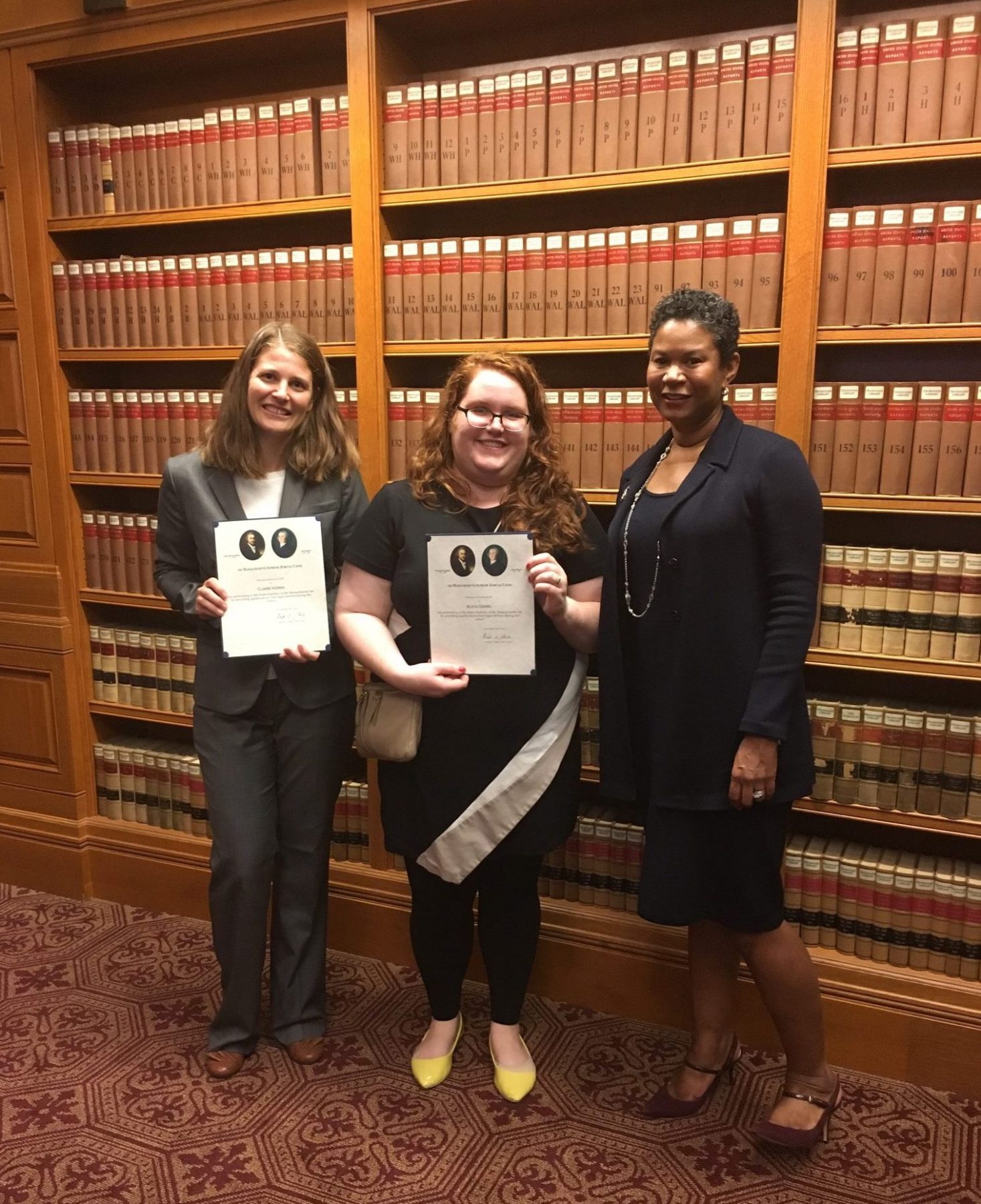 Photo of From left to right - Claire Horan JD 18, Alicia Daniel JD 18, and Justice Kimberly S. Budd standing in front of a book shelf