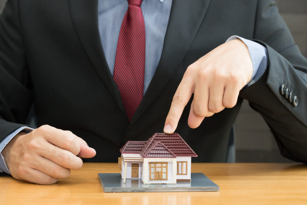Man in a suit puts his index finger on a small model house on a table.