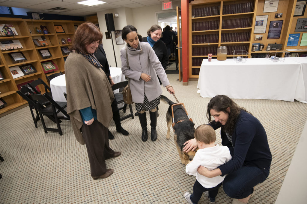 Julie McCormack and Haben Girma stand with a service dog as Dana Montalto crouches with a child,