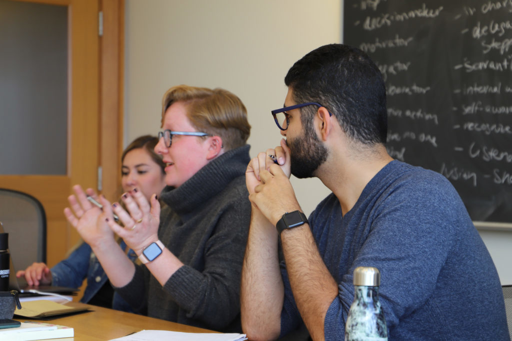 (From left to right) Fabiola Alvelais ’20, Jillian Rafferty ’20 and Daniel Moubayed ’20 sit in a classroom in front of a blackboard while Rafferty speaks.