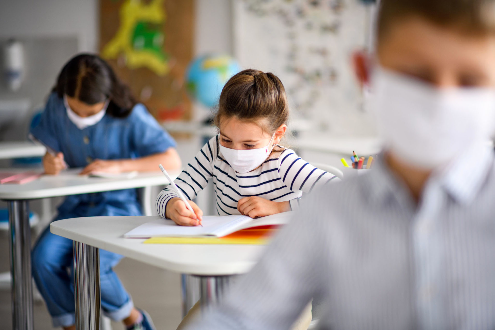Small children with face mask back at school after covid-19 quarantine and lockdown, writing.